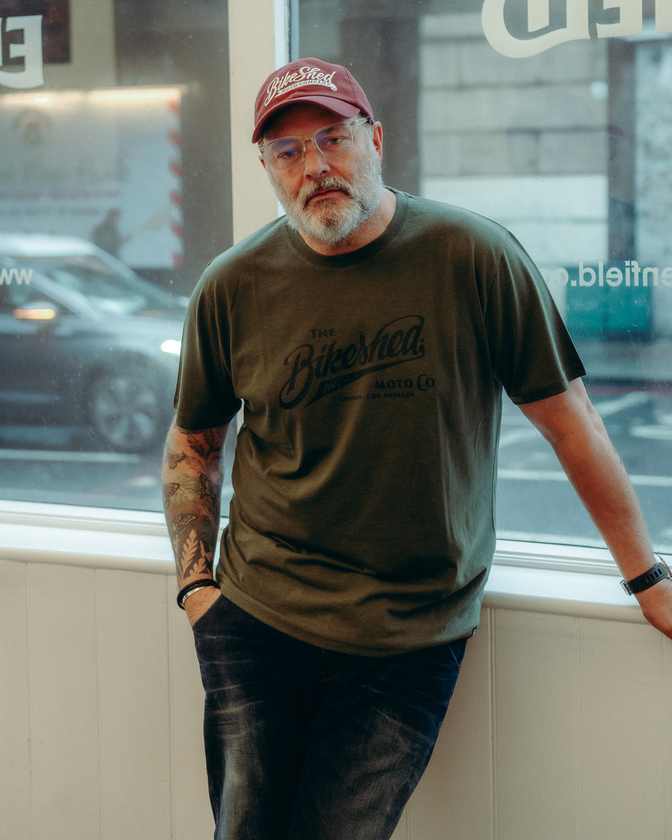 Model wearing Bike Shed Moto Co Inc T-Shirt Green in a white shop