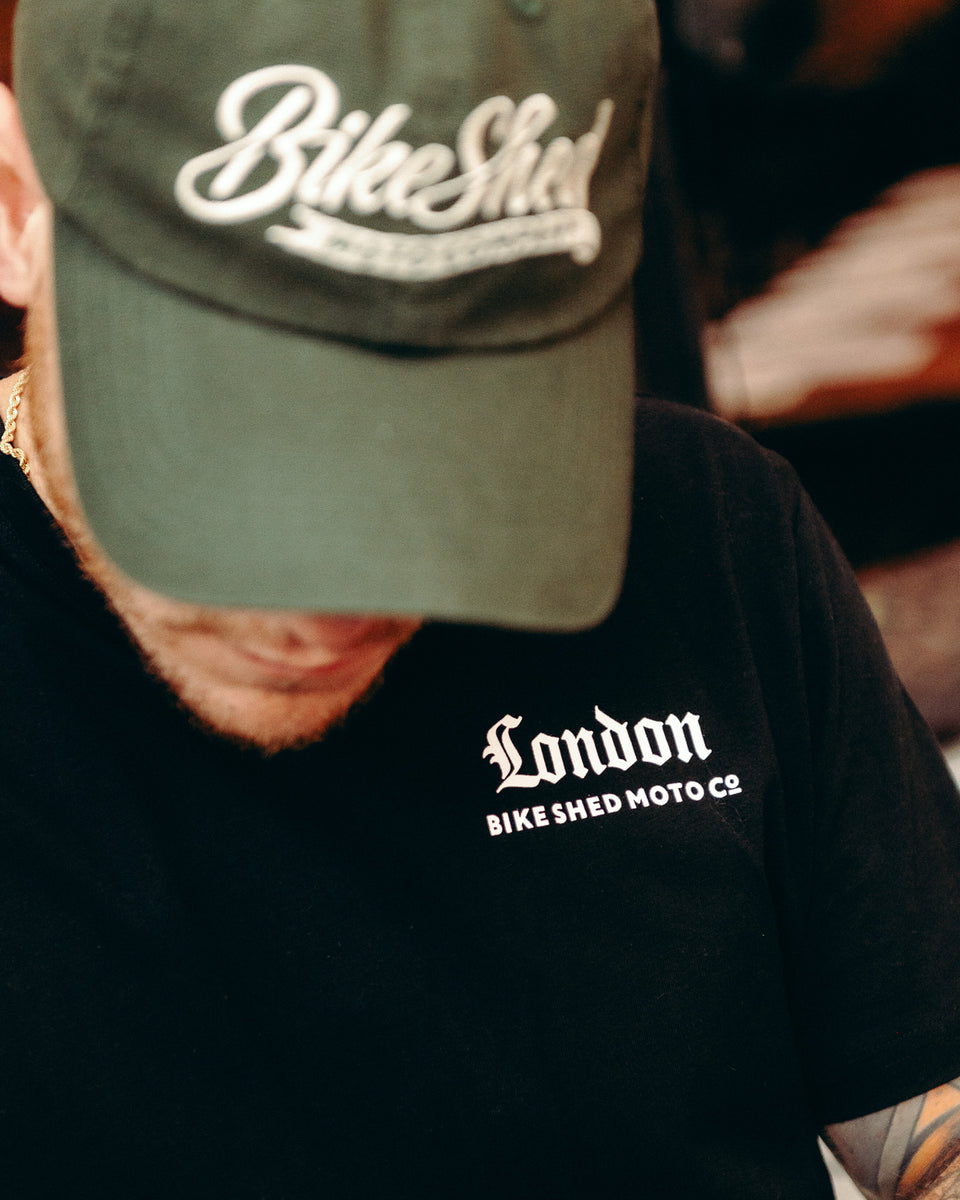 Model wearing black Bike Shed Moto Co Olde London Logo T Shirt while cutting hair in a barbershop