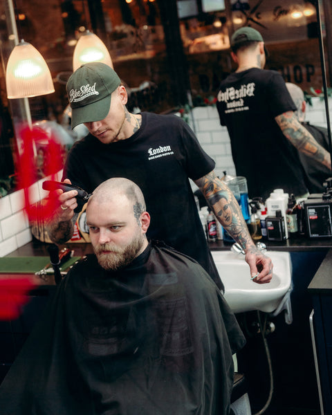 Model wearing black Bike Shed Moto Co Olde London Logo T Shirt while cutting hair in a barbershop