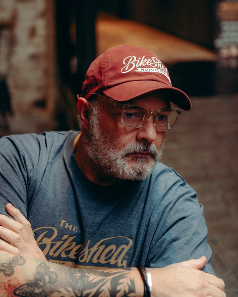 Model wearing Bike Shed Moto Script cap red sitting on brick driveway