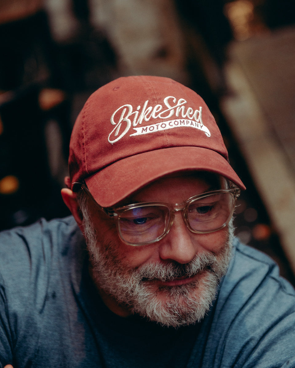 Model wearing Bike Shed Moto Script cap red sitting on brick driveway