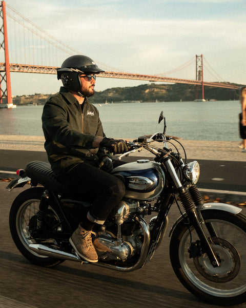 Model wearing the Bike Shed Moto Co. Twill Green logo jacket standing riding a motorcycle.