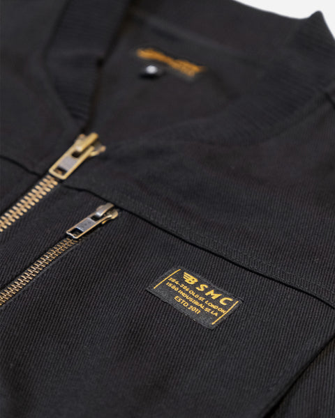 Black motorcycle vest with gold zipper and visible Bike Shed Moto Co brand logo on a white background