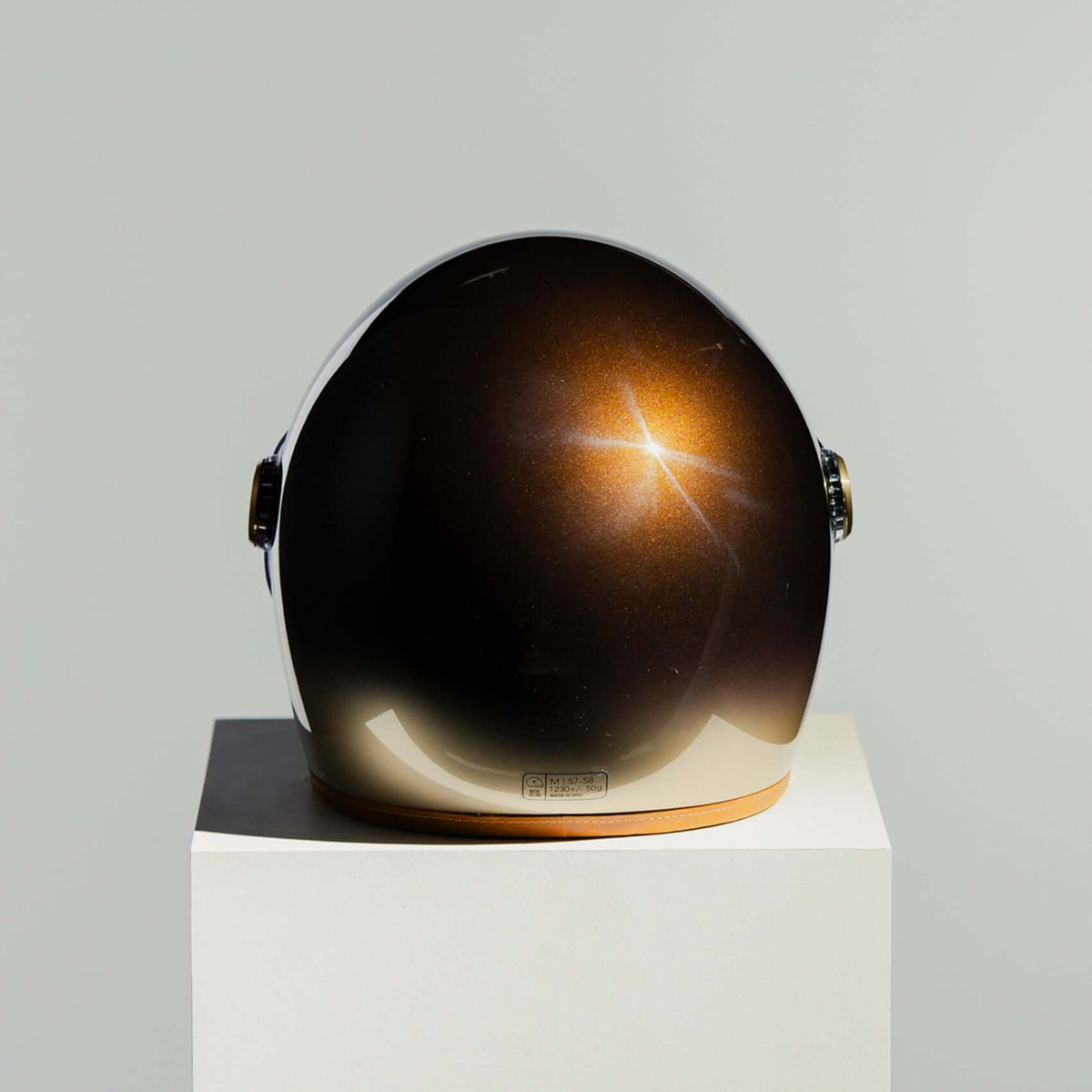 Helmet with reflective surface on a white pedestal against a light gray background